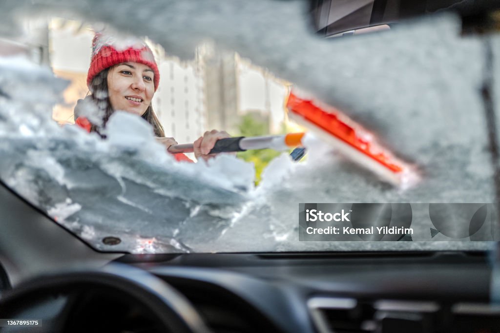 Millennial Woman in winter jacket scraping ice and snow from car windows Car Stock Photo