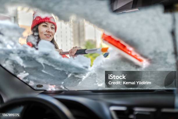 Millennial Woman In Winter Jacket Scraping Ice And Snow From Car Windows Stock Photo - Download Image Now