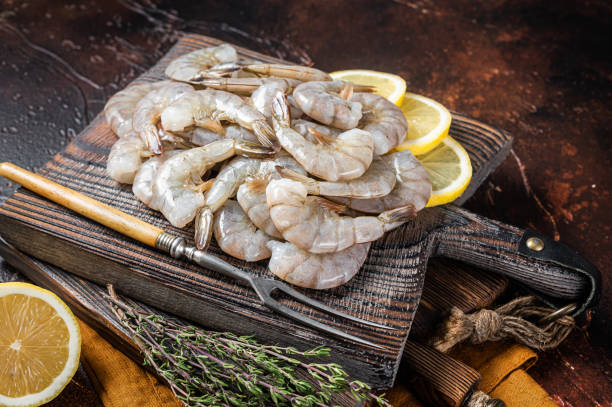 istock Raw tiger white shrimp prawn on board with herbs. Dark background. Top view 1367896206