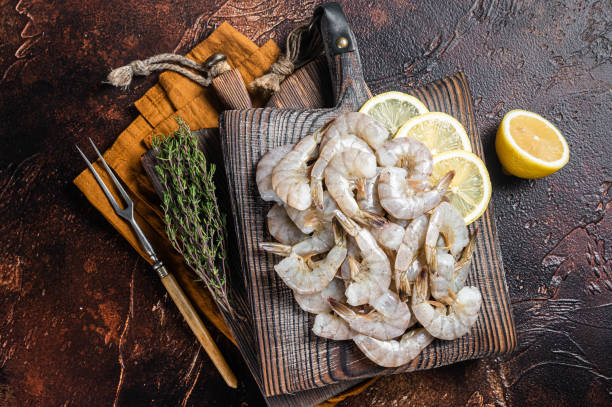 istock Raw tiger white shrimp prawn on board with herbs. Dark background. Top view 1367896214