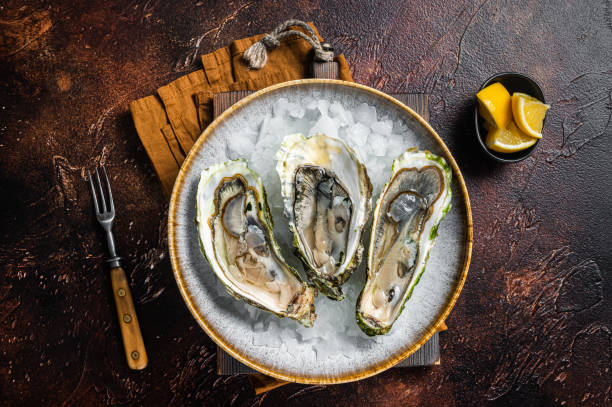 istock Opened Fresh oysters with lemon and ice in a plate. Dark background. Top view 1367896306