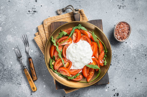 istock Italian cheese stracciatella burrata on plate with fresh tomatoes and arugula. Gray background. Top view 1367896369