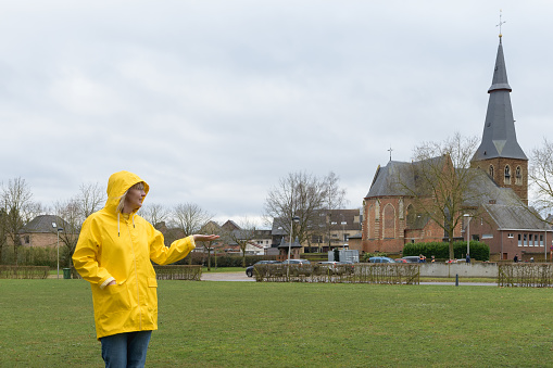 Waiting for the rain. Woman in a yellow raincoat on a grassy meadow against the backdrop of an old catholic church