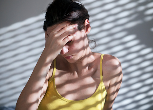Woman suffering from headache sitting on floor against a grunge wall with a striped shadow from the blinds