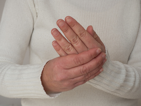 Mujer de mediana edad que sufre de dolor en las manos y masajea sus manos dolorosas aislando el fondo gris. Las causas de daño incluyen el síndrome del túnel carpiano, fracturas, artritis, ataque de gota o dedo en gatillo. photo