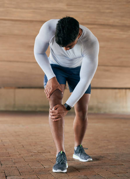 Shot of a sporty young man experiencing knee pain while exercising outdoors stock photo