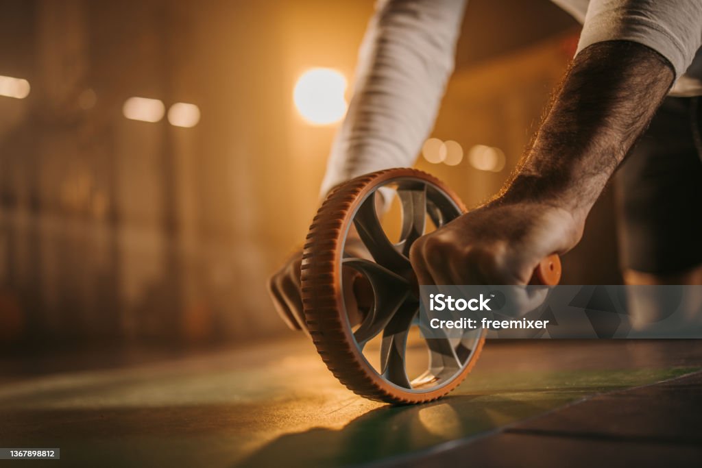 Exercise with ab roller Strong man gripping tight ab roller wheel while exercising on the floor in dark gym alone. Abdominal Toning Wheel Stock Photo