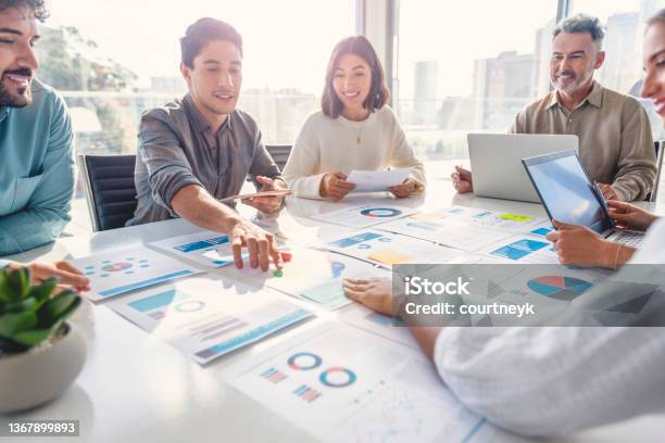 Multi Racial Diverse Group Of People Working With Paperwork On A Board Room Table At A Business Presentation Or Seminar The Documents Have Financial Or Marketing Figures Graphs And Charts On Them There Are Laptops And Digital Tablets On The Table Stock Photo - Download Image Now