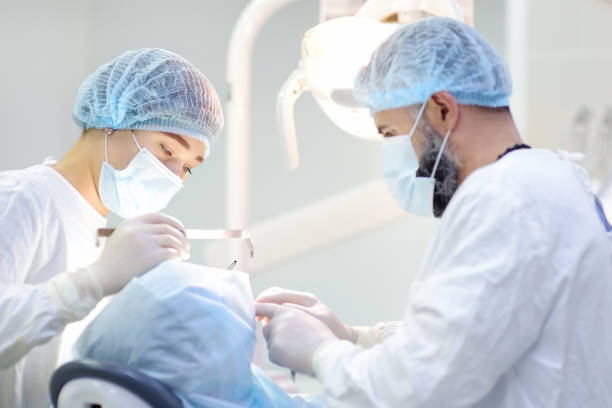 istock Surgeon and nurse during a dental operation. Anesthetized patient in the operating room. Installation of dental implants in the clinic. 1367902225