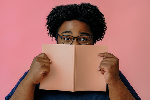african american man posing with a book in the studio over pink background