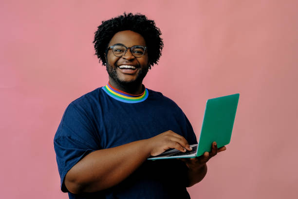 junger afroamerikaner posiert mit laptop im studio über rosa hintergrund - isolated cheerful businessman smiling stock-fotos und bilder