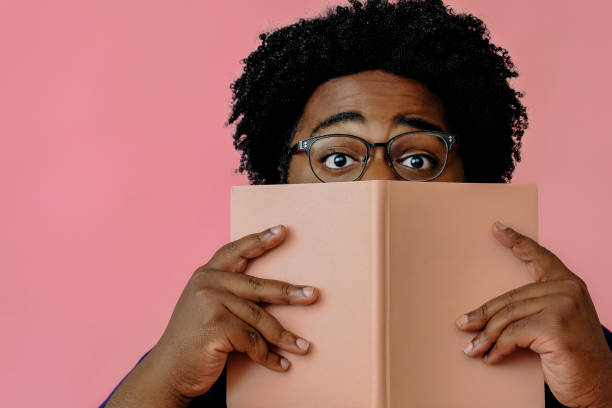 istock african american man posing with a book in the studio over pink background 1367902360