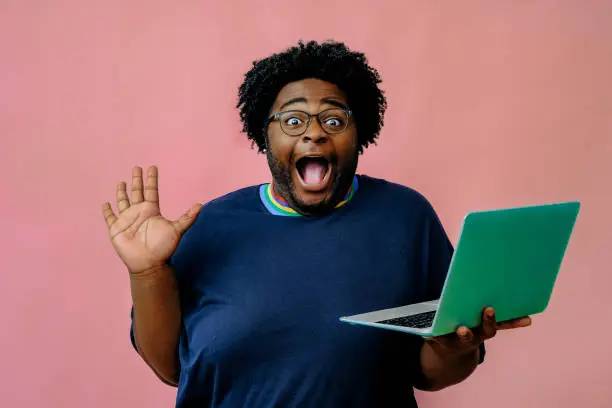 young african american man posing with laptop in the studio over pink background