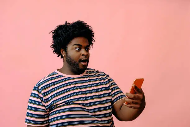 young african american man with a phone posing in the studio over pink background