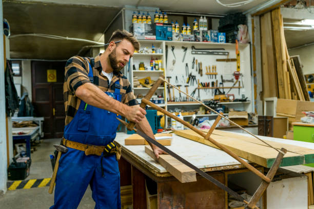 istock Handsome young carpenter cutting the board using the old carpenter saw 1367902789