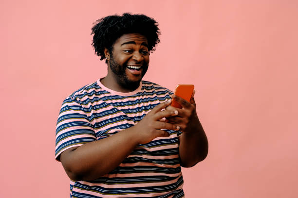istock young african american man with a phone posing in the studio over pink background 1367903988