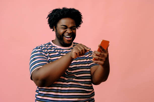 istock young african american man with a phone posing in the studio over pink background 1367904001
