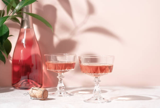 deux verres en cristal de vin mousseux rose ou de champagne sur une table en marbre rose pastel au soleil. composition créative avec espace de copie. - table on wine alcoholism photos et images de collection