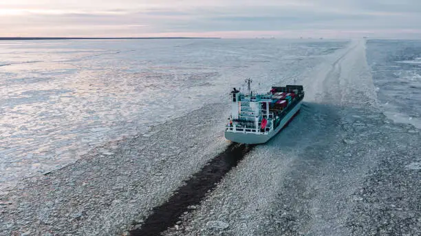 Photo of A large sea vessel with containers is moving in the ice on the sea