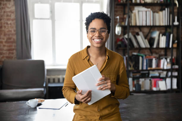 портрет радостной молодой афроамериканки, держащей в руках цифровой планшет. - women dependency business time стоковые фото и изображения