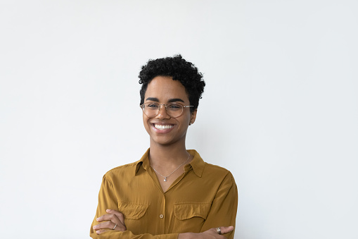 Head shot portrait of smiling beautiful confident young African American woman in eyeglasses standing with folded arms, isolated on white studio wall background, professional career concept.