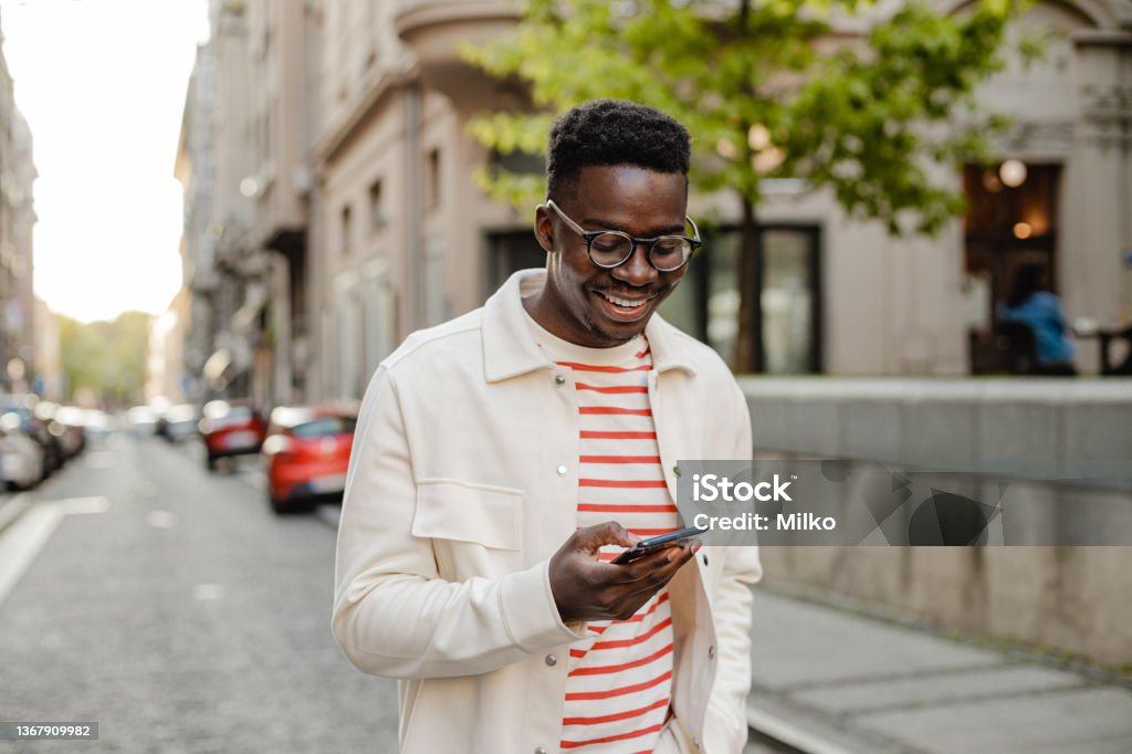 Young African-American man uses a mobile phone on the go The portrait of an African-American man is on the street, he is walking and using a mobile phone on the go Using Phone Stock Photo