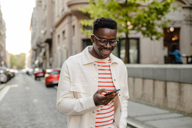Young African-American man uses a mobile phone on the go The portrait of an African-American man is on the street, he is walking and using a mobile phone on the go happy using phone stock pictures, royalty-free photos & images