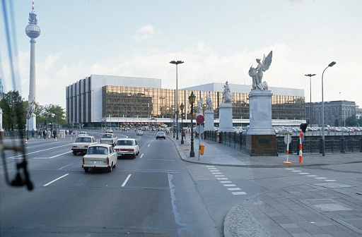 Berlin (East), GDR, Germany, 1988. Street scene at the Schlossbrücke with the former Palace of the Republic and the television tower. Also: cars (Trabi), pedestrians and the famous Schlossbrücken figures.