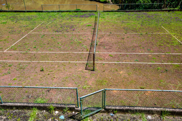 Aerial top down view of a red, empty tennis court on a sunny day.