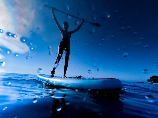 Adult Woman Standing on Paddleboard and Holding Paddle Above Her Head Adult Woman Standing on Paddleboard and Holding Paddle Above Her Head. paddleboard surfing water sport low angle view stock pictures, royalty-free photos & images