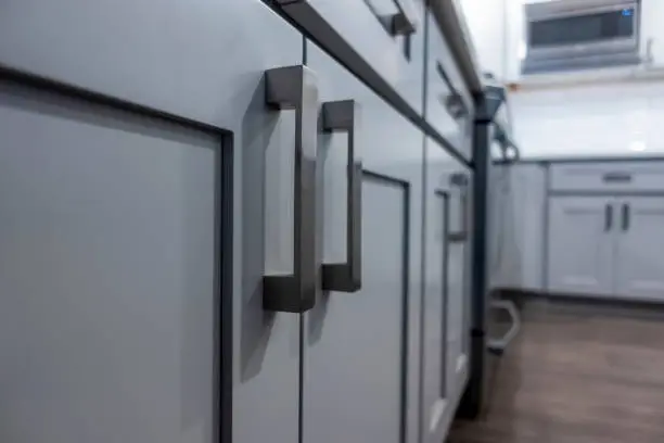 Photo of Low angle view of gray kitchen cabinet door handles inside a large, beautiful kitchen with finished, hardwood floors