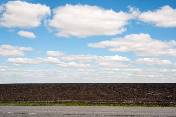 Blue sky with white clouds on a background of plowed field and gray asphalt road