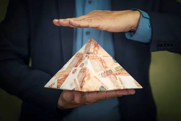 Photo of pyramid scheme in the hands of a fraudster. The concept of exchange in financial markets is the collapse of the financial system of capitalism.