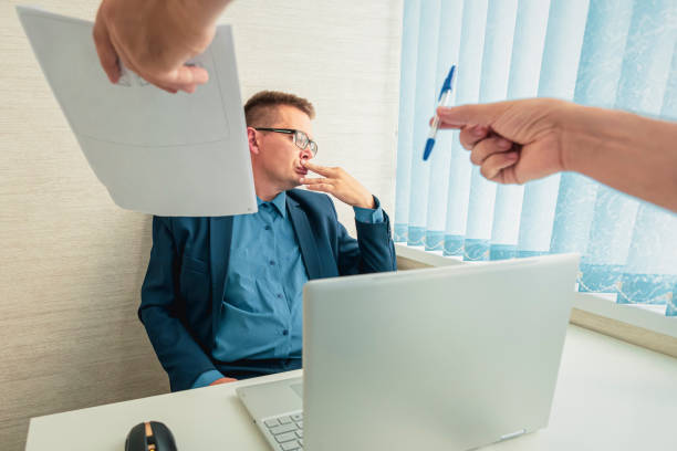 sad businessman in a suit sits in the office and looks at the documents. conclusion of a contract with the boss. unwillingness to sign a contract. dismissal of an employee. - unwillingness imagens e fotografias de stock