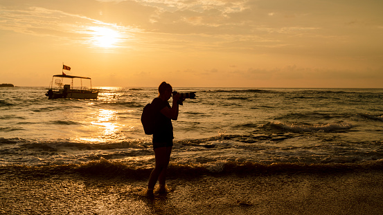Silhouette of the woman, traveler, and photographer filming boats in the ocean at the sunset.