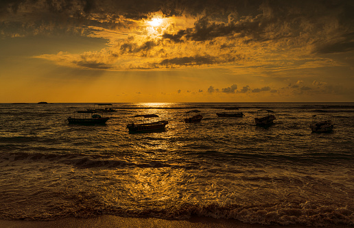 Fishing boats on moorage nearby shore in the ocean in Hikkaduwa, Sri Lanka at the sunset.