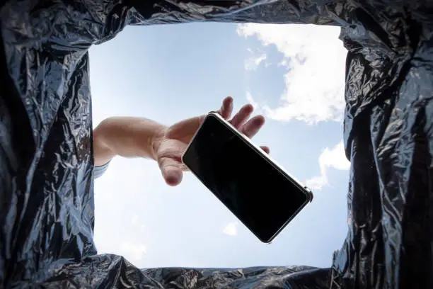 Photo of man throws a non-working smartphone into a trash can. Bottom view from the trash can. The problem of recycling and pollution of the planet with garbage.