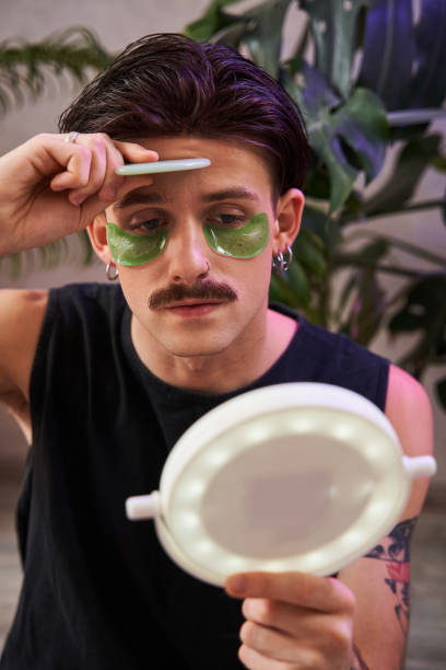 istock Serious man using facial gua sha jade board while looking at the mirror at his reflection 1367930129