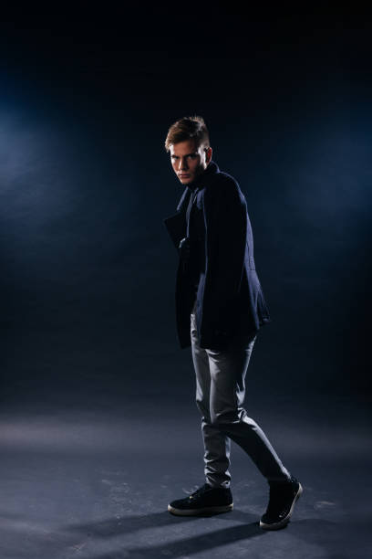 istock Portrait of a handsome with sharp jawline young man wearing a scarf while posing inside a studio on a black background. 1367940258