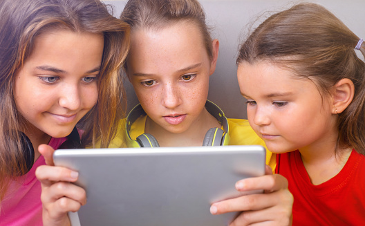 Child and teenagers look at the same tablet together on the same sofa