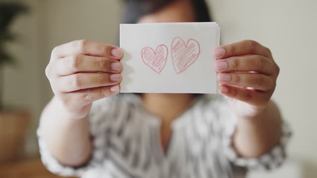Woman showing a white paper with coloring red heart shape by crayon