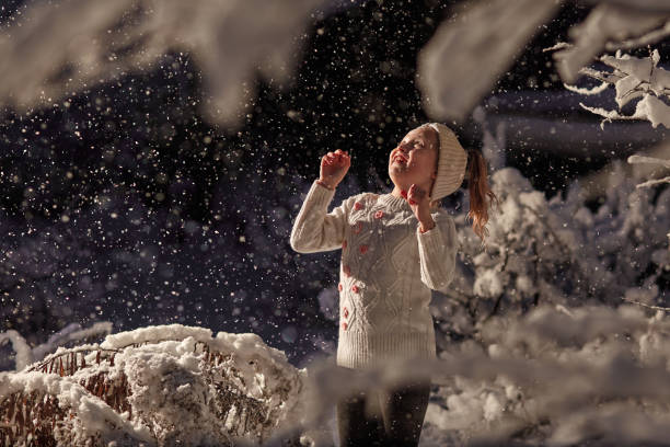 little girl in white sweater and blue hair in snow catches snowflakes dark night background