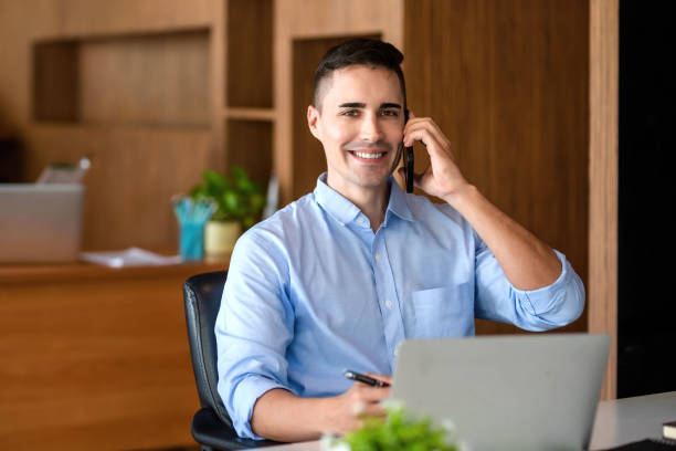 Charming businessman smiling talking on the mobile phone in the office. Looking at camera. stock photo