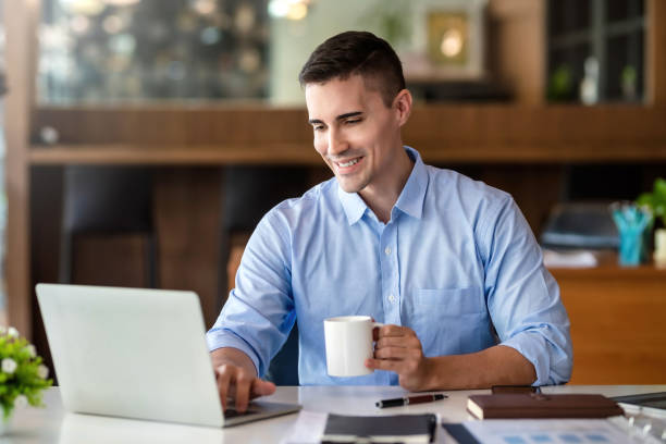 istock Businessman holding a coffee mug working on laptop at office. 1367946285