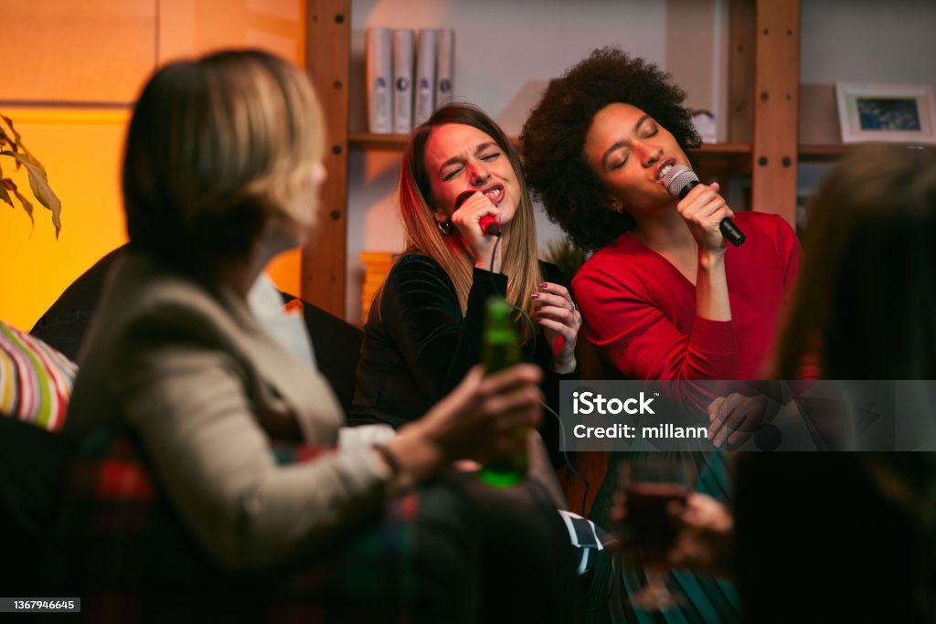 Happy multicultural friends sitting at home, laughing, singing, and having fun on karaoke night. Karaoke Stock Photo