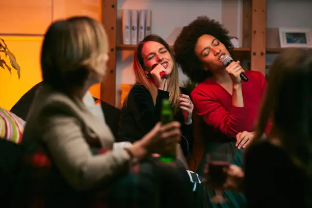 Photo of Happy multicultural friends sitting at home, laughing, singing, and having fun on karaoke night.