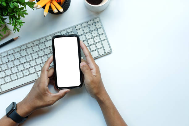 istock Young man holding smart phone with empty screen on white office desk. 1367949845
