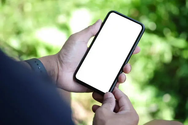 Photo of Young man using smart phone while sitting in the park. Blank screen for advertisement.