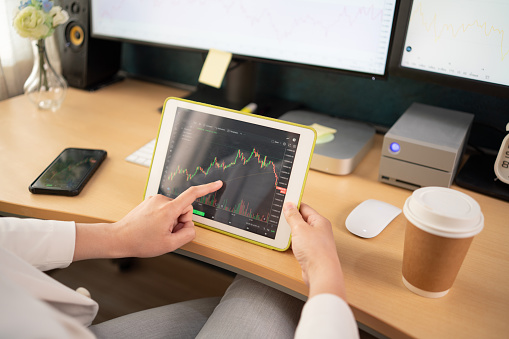 Asian stock investors Wearing a white suit In the bedroom of the house View stock charts on the computer screen and tablet.