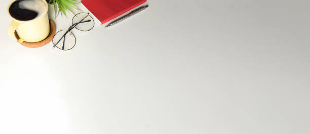 istock Minimal workplace with eyeglasses, coffee cup, notebook and houseplant on white table with copy space. 1367949960
